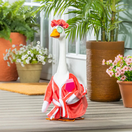 A duck dressed in a pink outfit stands on a porch, showcasing its unique attire against a cozy background.