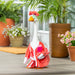 A duck dressed in a pink outfit stands on a porch, showcasing its unique attire against a cozy background.