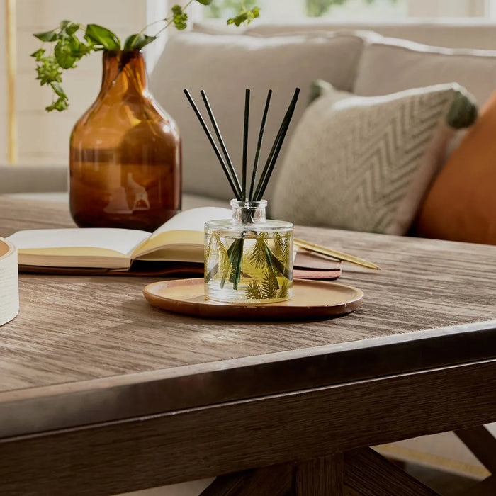 A diffuser with reeds on a wooden table in a cozy living room setting.