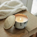 Candle in a decorative container with a wooden lid on a wooden surface