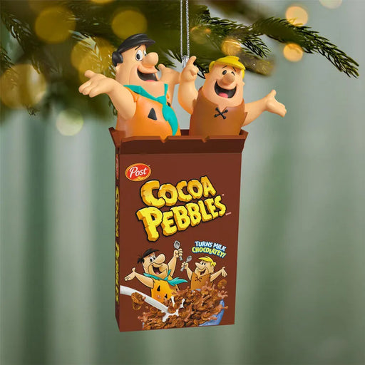Glossy plastic 2026 Cocoa Pebbles Flintstones ornament hanging on silver chain against blurred holiday lights