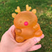 Hand holding a transparent orange reindeer-shaped object with a pink nose against a blurred green grass background