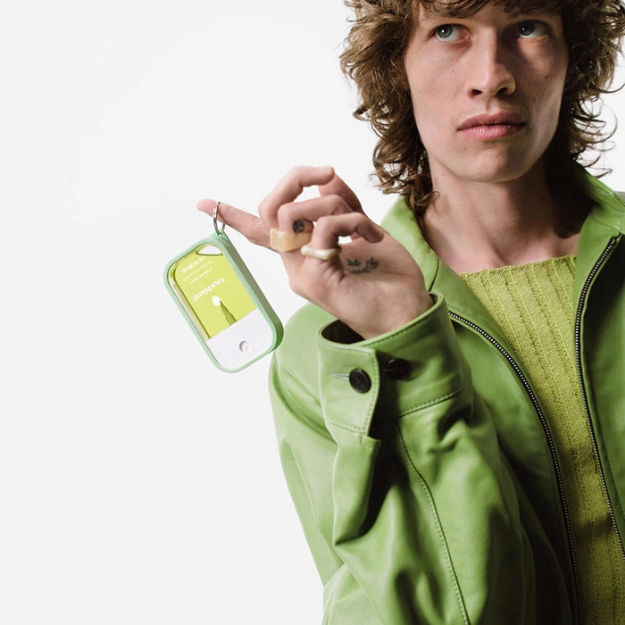 Model holding Touchland Power Mist in green silicone keychain case.