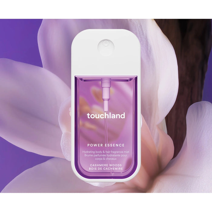 Touchland Cashmere Woods Body Mist Power Essence bottle held by a hand with a purple background