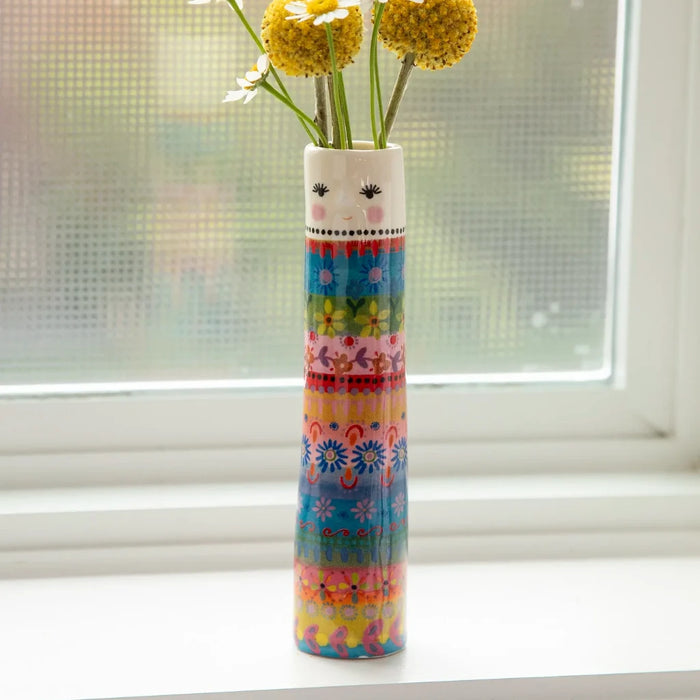 A decorative vase with blooming flowers rests on a window sill, illuminated by natural light.