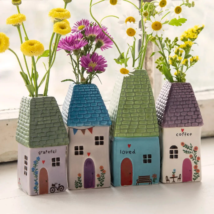 A quaint house featuring a vase of daisies on the window sill, adding charm and color to the scene.