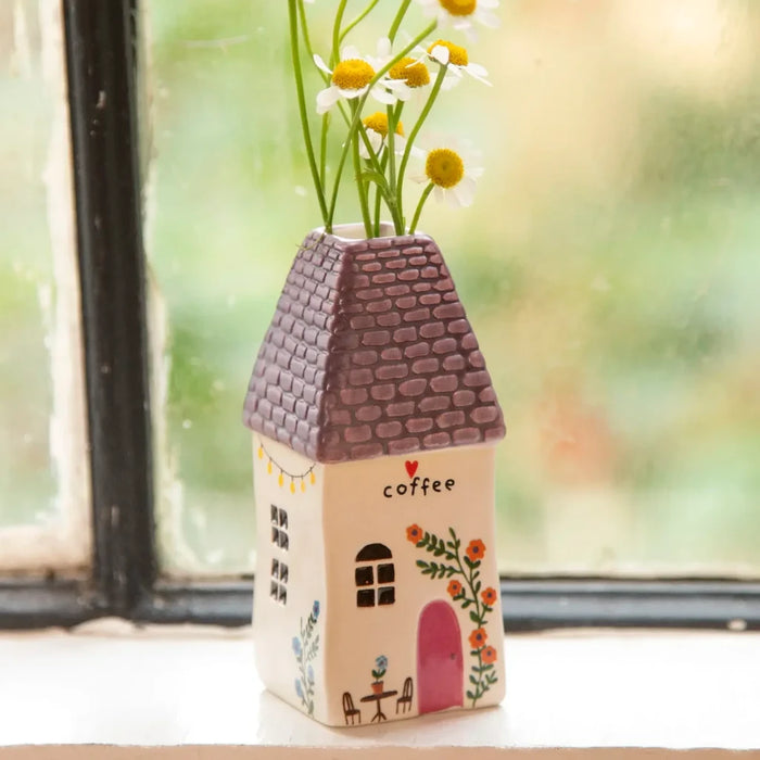A small house adorned with a vase of daisies on the window sill, showcasing a cheerful and welcoming vibe.
