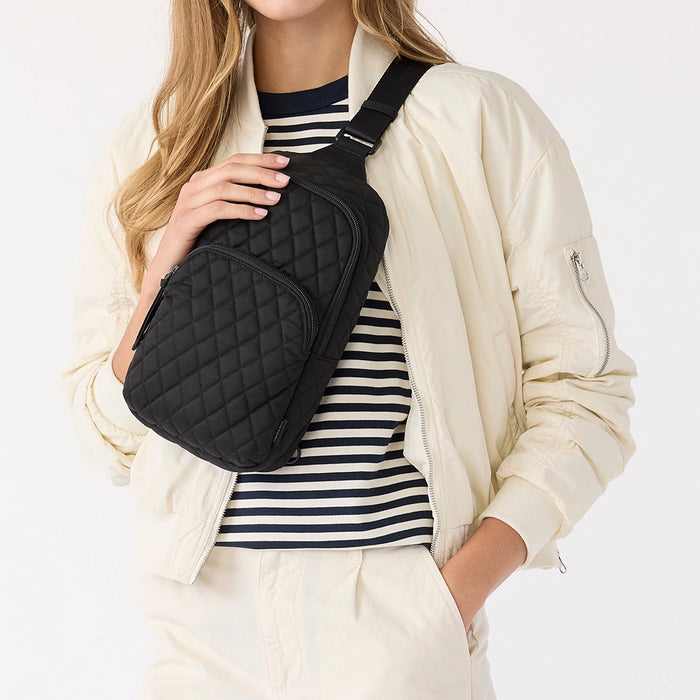 Model wearing Vera Bradley Lorman Sling Backpack in Moonless Night crossbody style with striped shirt and cream jacket.