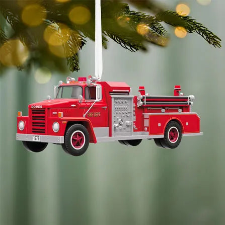 Red 1973 Dodge fire engine ornament hanging on evergreen branch with golden lights