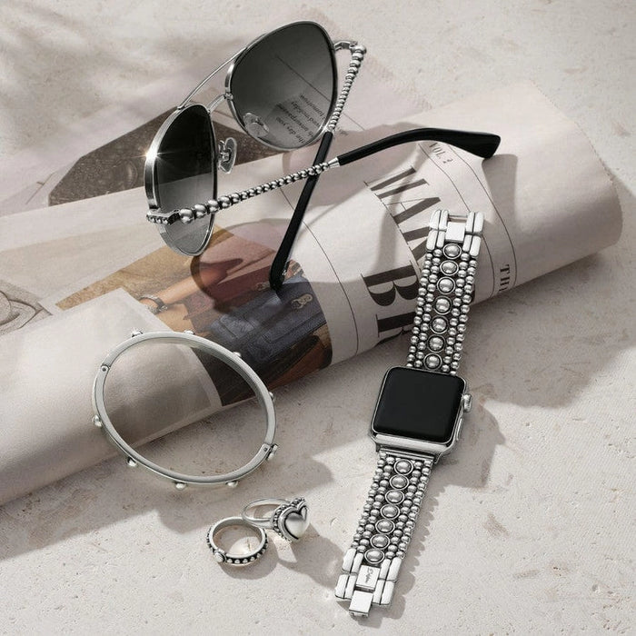 Silver watch with decorative band, sunglasses, and ring on a light surface