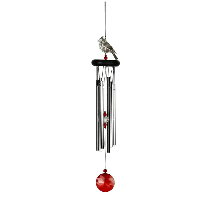 A vibrant red and white bird sits beside a wind chime, creating a serene outdoor scene.