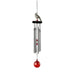 A vibrant red and white bird sits beside a wind chime, creating a serene outdoor scene.
