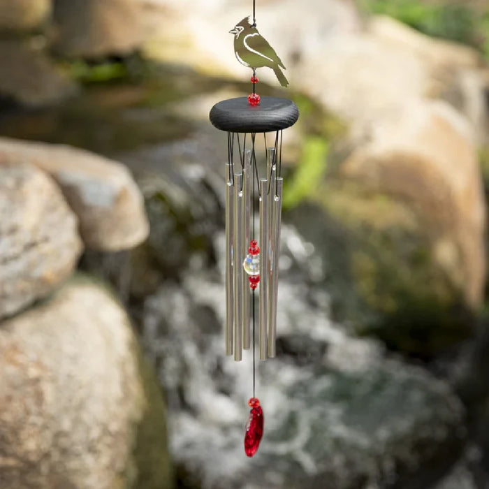 A red and white bird is positioned next to a wind chime, adding charm to the tranquil setting.