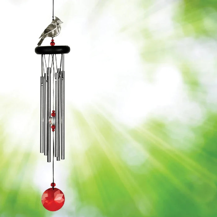 A red and white bird alongside a wind chime, enhancing the peaceful ambiance of the garden.