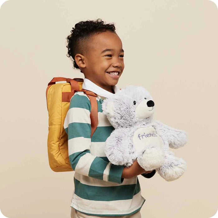 Child holding Warmies Friends Bear Plush while wearing a backpack, showing plush bear as a comforting companion