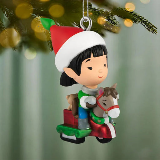 Christmas ornament of a child with a horse and Santa hat hanging on a tree.