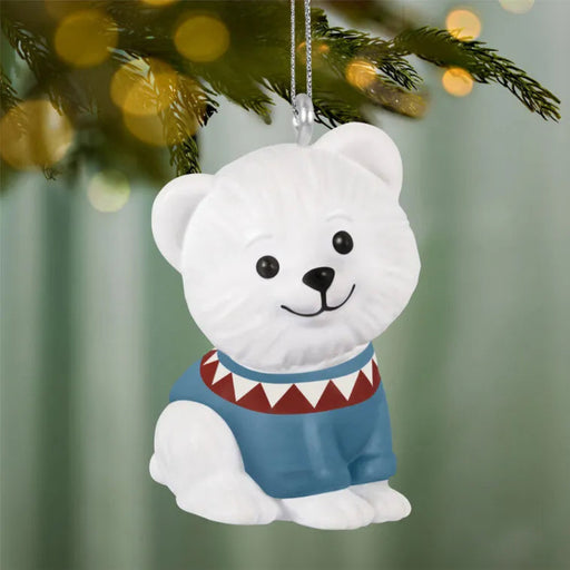 White polar bear ornament with a blue sweater hanging on a Christmas tree.
