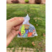 Hand holding a small transparent bag with colorful wiggletz against a grassy background