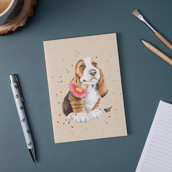 Wrendale Designs Basset Hound small notebook with dog and flower illustration shown on desk with pen, pencils, and coffee