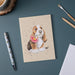 Wrendale Designs Basset Hound small notebook with dog and flower illustration shown on desk with pen, pencils, and coffee