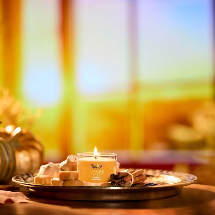 Yankee Candle Golden Pumpkin Mini lit on a tray with cookies and cinnamon sticks, warm golden background.