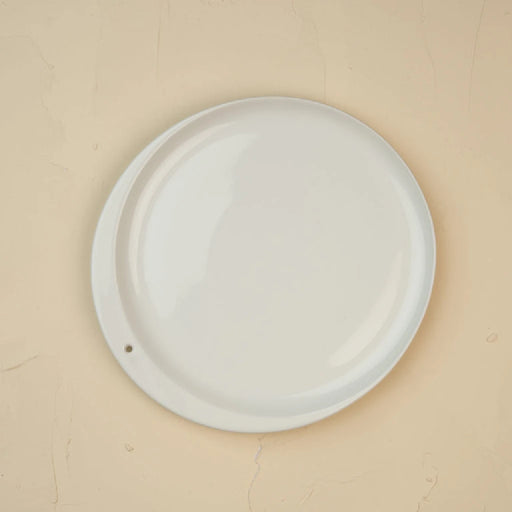 A white plate displayed against a beige wall, highlighting its simplicity and elegance.
