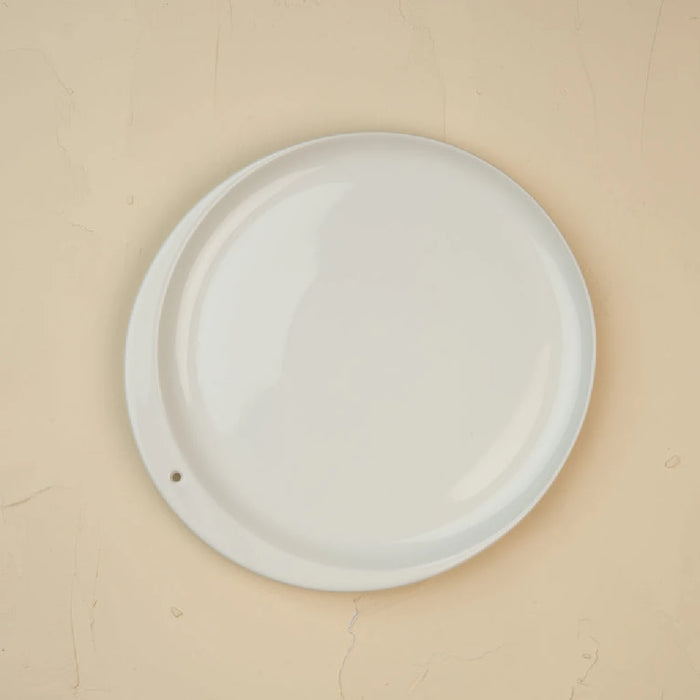A white plate displayed against a beige wall, highlighting its simplicity and elegance.