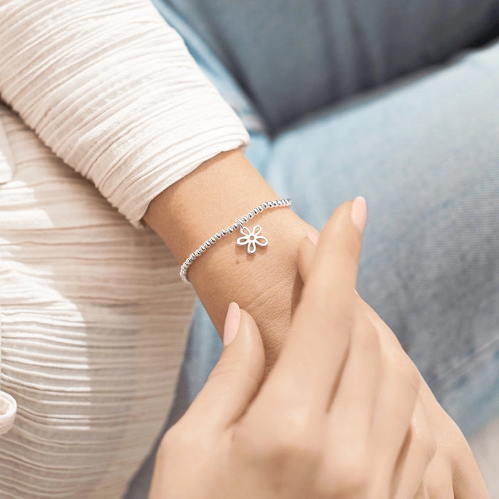 A Littles & Co Thinking Of You bracelet worn on wrist featuring a silver beaded stretch band and delicate flower charm