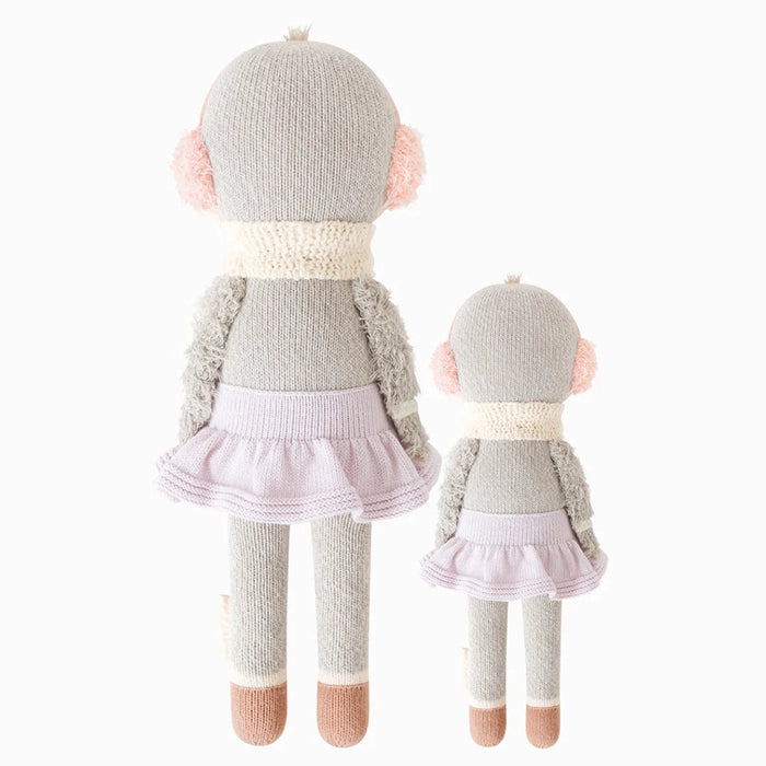 Back view of two Cuddle + Kind Skylar the Penguin dolls, one regular size and one little, both wearing lavender knit skirts, white scarves, and pink earmuffs.
