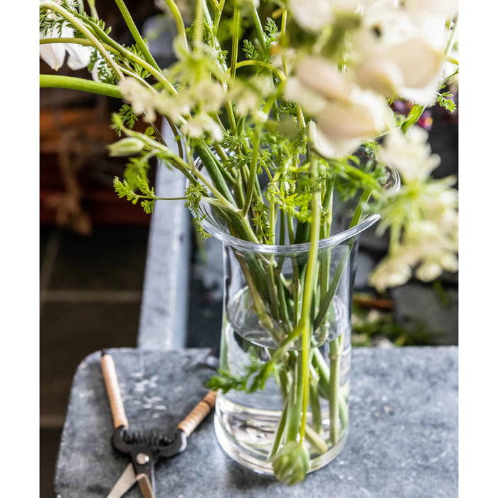 A clear vase containing water and fresh green leaves, positioned on a simple table.