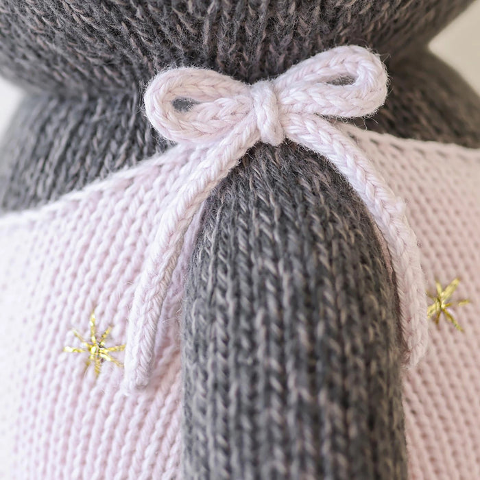 Close-up of pink knit bow and golden embroidered stars on Nova the Kitten’s overalls by Cuddle + Kind.
