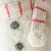 Close-up of baby snowman’s candy cane striped scarf and black button details on soft knit fabric.