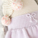Close-up of Skylar the Penguin doll’s lavender knit skirt waistband with a small knitted bow detail.