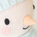 Close-up of Spruce the Snowman’s embroidered face, showing black eyes, a smile, pink cheeks, and a crocheted carrot-shaped nose.