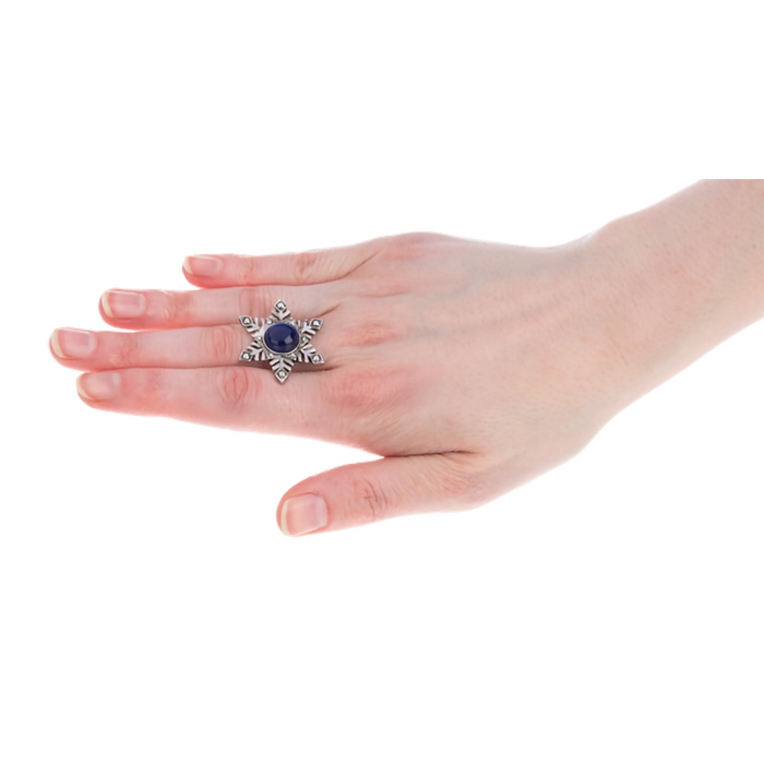 Hand wearing a decorative ring with a blue gemstone on a white background