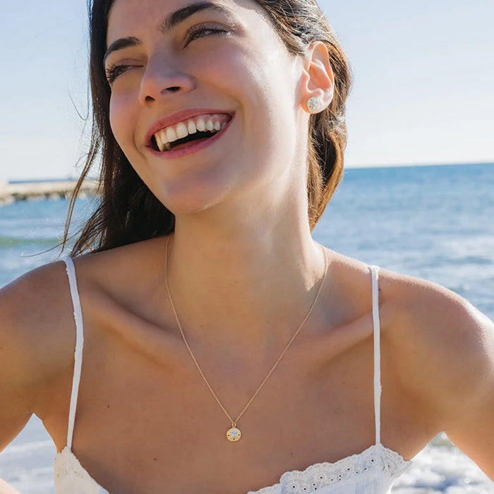 Smiling Women Wearing a White Sapphire Sand Dollar Necklace on a beach