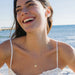 Smiling Women Wearing a White Sapphire Sand Dollar Necklace on a beach