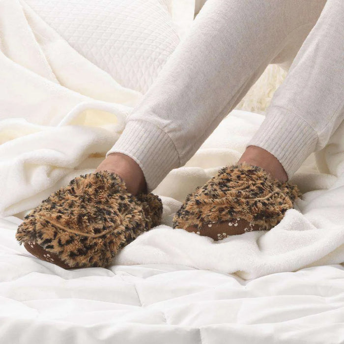 Person wearing brown fuzzy slippers on a white bed