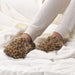 Person wearing brown fuzzy slippers on a white bed