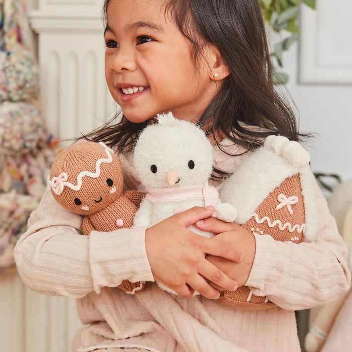 Child holding Cuddle + Kind Baby Snowman in Blush Pink with Gingerbread Doll and Gingerbread House plush toys.