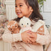 Child holding Cuddle + Kind Baby Snowman in Blush Pink with Gingerbread Doll and Gingerbread House plush toys.