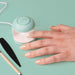 Hand with painted nails using a small UV Nail Lamp on a light green background