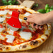 Person using a pizza cutter on a pizza with red sauce and cheese