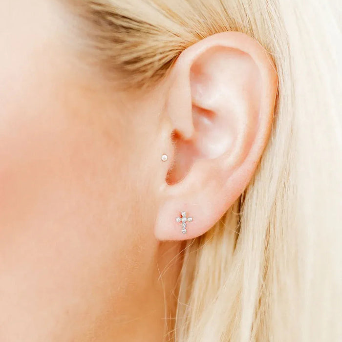 Close-up of an ear with gold stud earrings against a blurred background