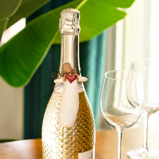 Decorative bottle with a figurine and heart-shaped object, surrounded by wine glasses on a table.