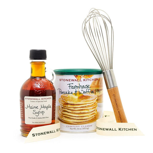 A gift set from Stonewall Kitchen including a bottle of Maine maple syrup, a container of farmhouse pancake and waffle mix, and a stainless steel balloon whisk, all displayed on a white background.